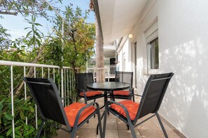 An outdoor patio with a round table and four chairs, surrounded by greenery and a white building. - Apartments Mirjana (Marina)