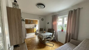 Ένας μικρός, λειτουργικός χώρος διαβίωσης με τραπεζαρία, μικρή κουζίνα και ένα παράθυρο με κουρτίνες.