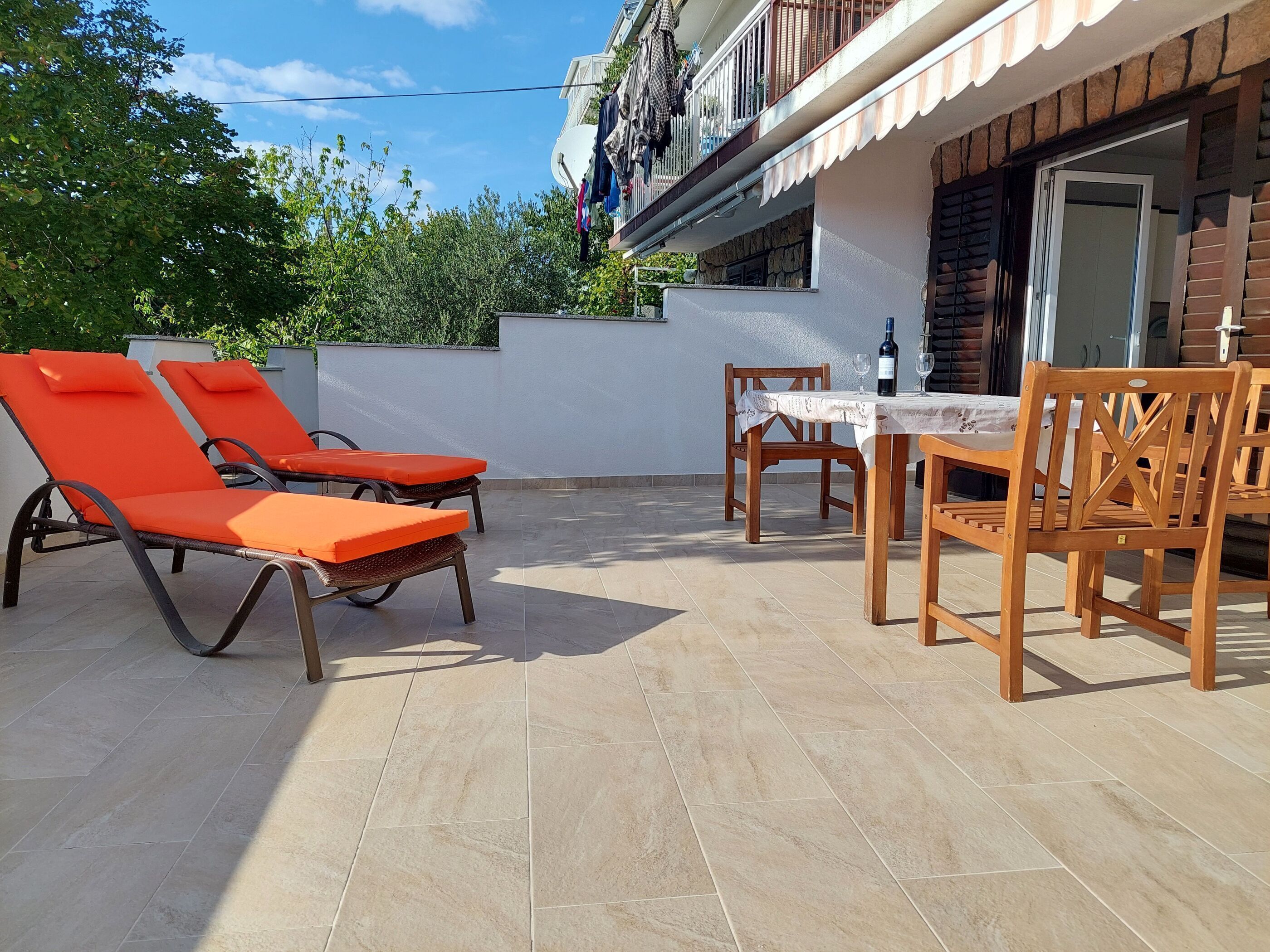 A patio with two orange lounge chairs, a wooden table with chairs, and a satellite dish on the building.
