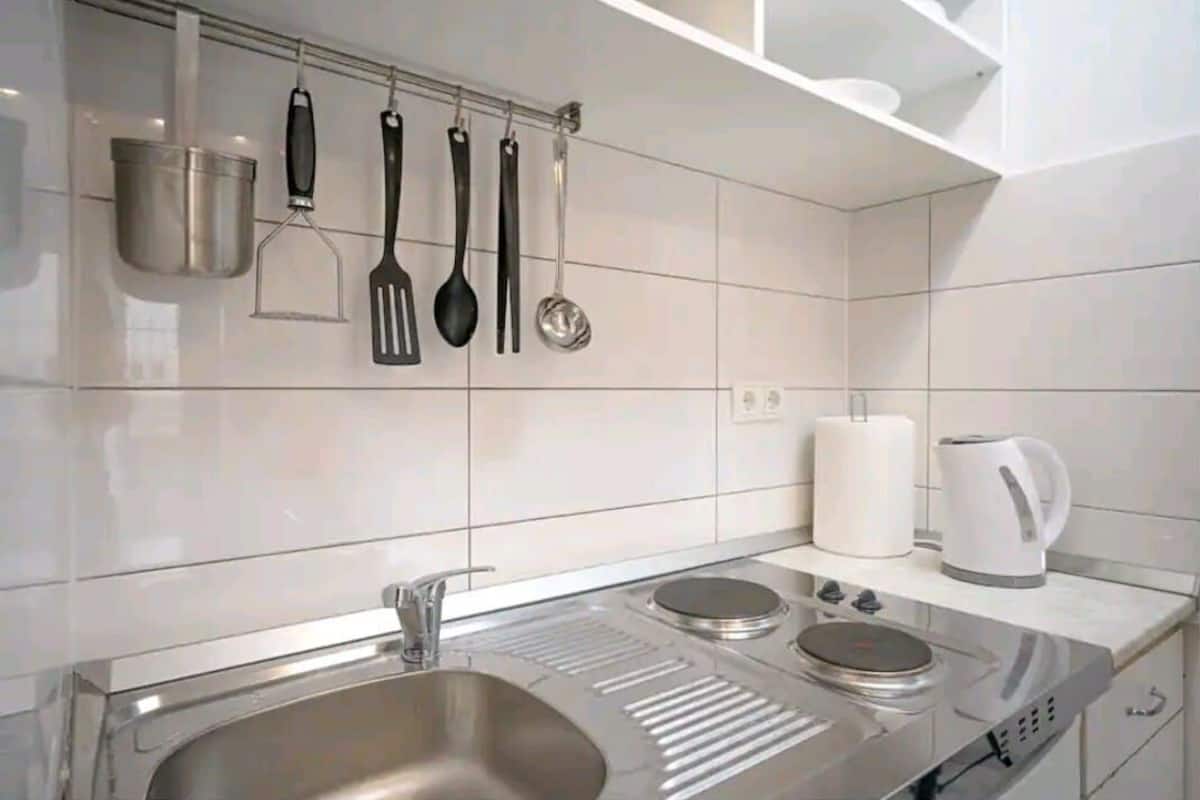 A modern kitchen with a stainless steel sink, a built-in stovetop, and hanging utensils.