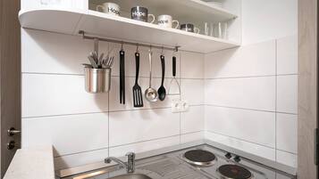 A kitchen with white tiled walls, a stainless steel sink, and a stove. There are utensils hanging on a rack above the sink.