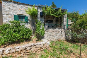 Un edificio in pietra dall'aspetto rustico, con un piccolo balcone e una finestra con persiane verdi.