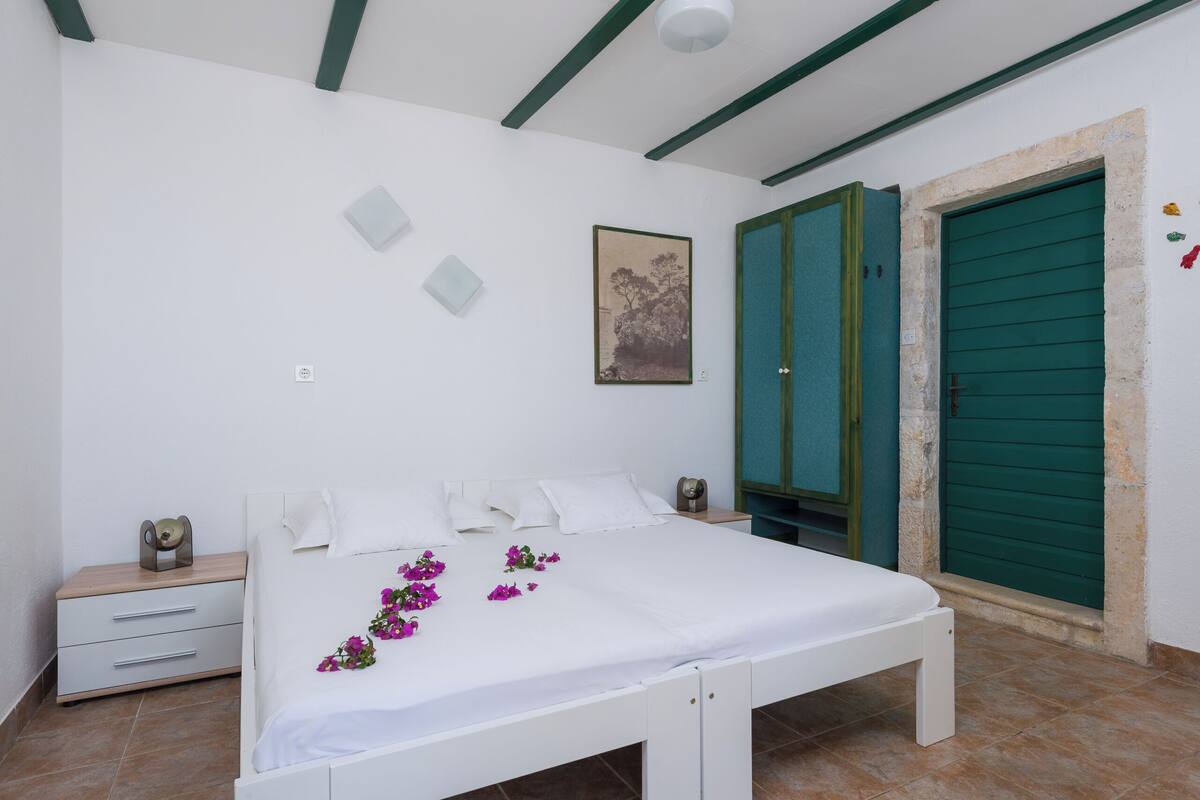 Une chambre à coucher avec un lit, une table de chevet, une porte verte et un tableau encadré au mur.