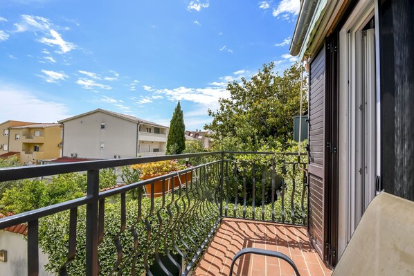 A balcony with a metal railing, potted plants, and a view of neighboring buildings and trees. - Apartment Sasa (Kastela)