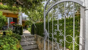 A gated entrance with a stone wall and metal gate, leading to a staircase and a building with a yellow facade. - Apartment Sasa (Kastela)