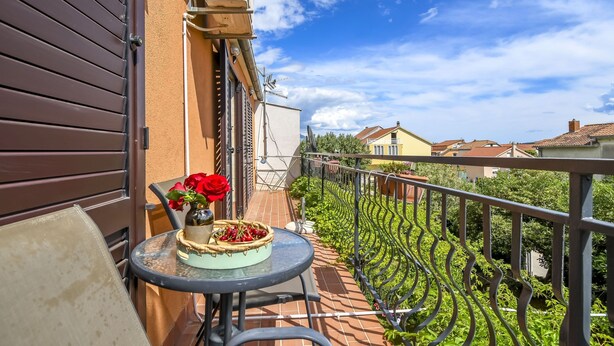 A balcony with a table, a vase with red flowers, and a basket of cherries. - Apartment Sasa (Kastela)