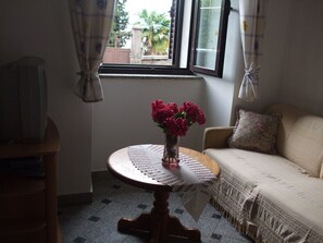 A room with a round wooden table, a beige sofa, and a window with curtains. - Apartments Vesna (Opatija)
