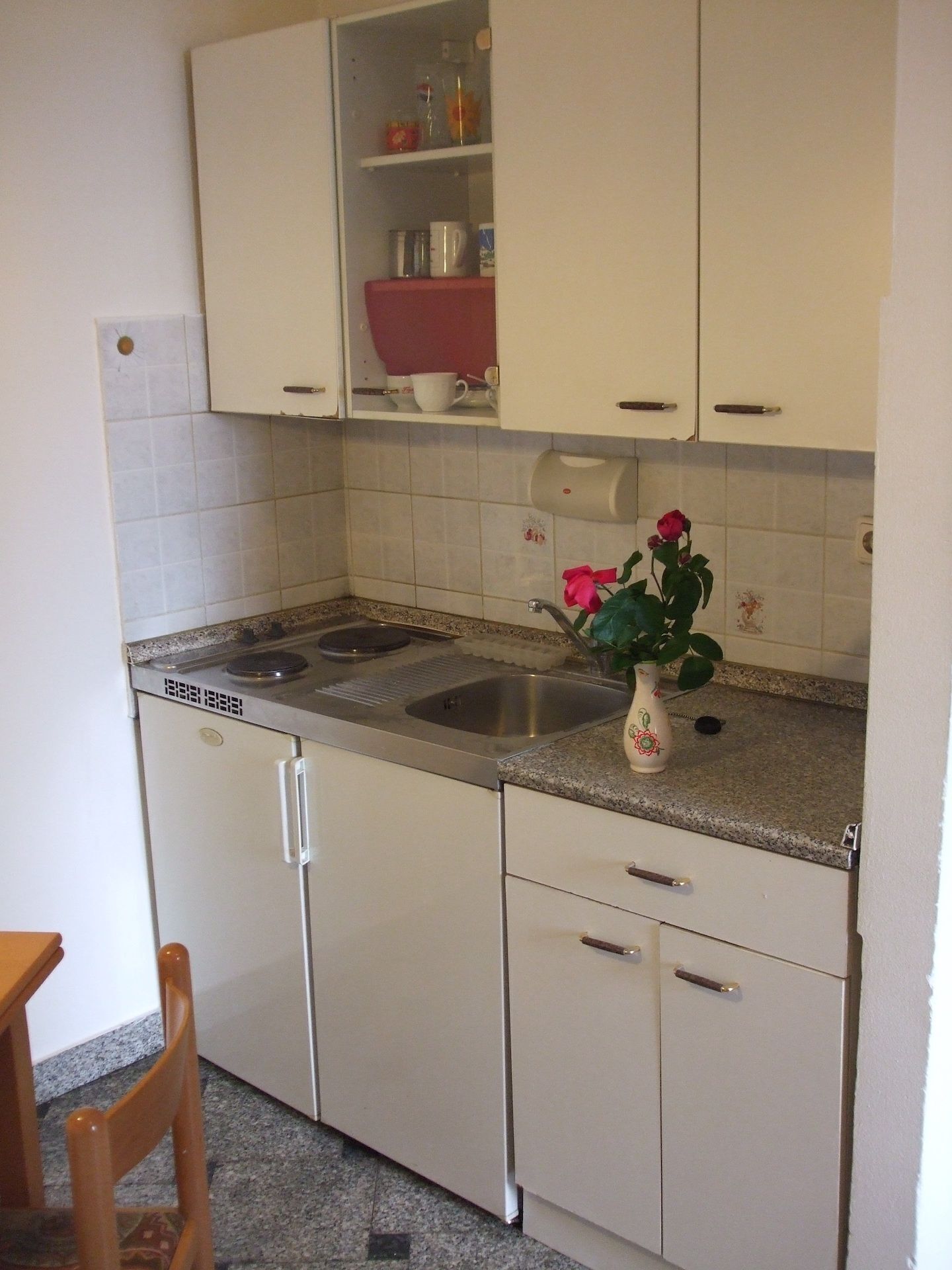 Eine Küche mit weißen Schränken, einer Edelstahl-Spüle und einem Blumenstrauß auf der Arbeitsplatte.