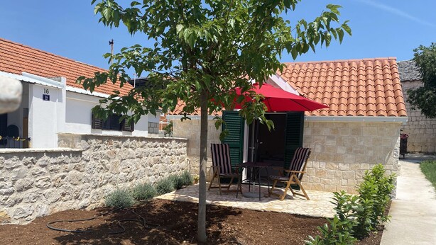 Eine Terrasse mit Steinmauer, einem Baum und einem roten Sonnenschirm.