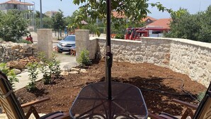 Eine Terrasse mit rundem Tisch, zwei Stühlen, einem Sonnenschirm und einer Steinmauer im Hintergrund.