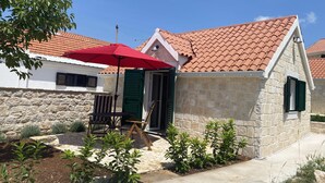 Ein Steinhhaus mit Ziegeldach, einem roten Regenschirm und einer kleinen Terrasse mit Tisch und Stühlen.