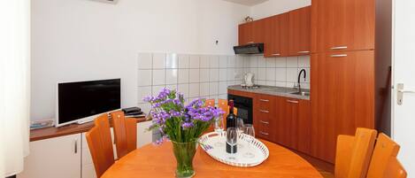 A modern kitchen with wooden cabinets, a dining table with chairs, a vase of flowers, and a tray with glasses and a bottle.