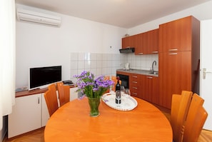 A modern kitchen with wooden cabinets, a dining table with chairs, a vase of flowers, and a tray with glasses and a bottle. - Apartments Marino (Omis)