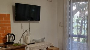Une chambre avec un téléviseur fixé au mur, une table avec une chaise, une bouilloire et une bouteille d’eau.