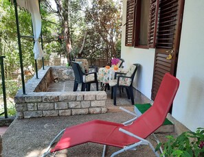A patio area with a table and chairs, a red lounge chair, and a stone wall. - Apartments Mala Kuca Kraj Mora (Sibenik)