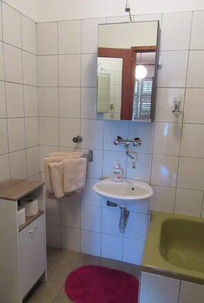A bathroom with a white sink, a mirror, a towel rack, and a red rug. - Apartments Mala Kuca Kraj Mora (Sibenik)