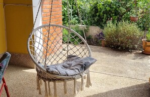 A wicker chair with a cushion in a covered outdoor area with a brick wall and potted plants. - Apartments Mala Kuca Kraj Mora (Sibenik)