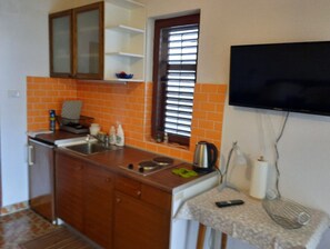 Una cocina compacta con encimera de madera, horno integrado, lavamanos y ventana con persianas.