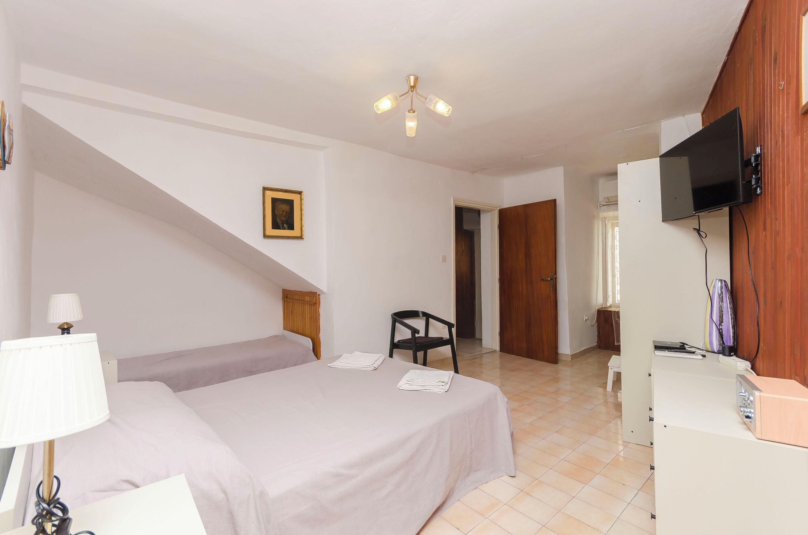 A bedroom with a bed, a chair, a desk, a television, and a ceiling fan.