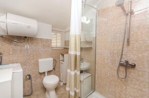 A bathroom with a toilet, sink, shower, and a white toilet paper holder. - Apartments Nautical Nest (Tribunj)