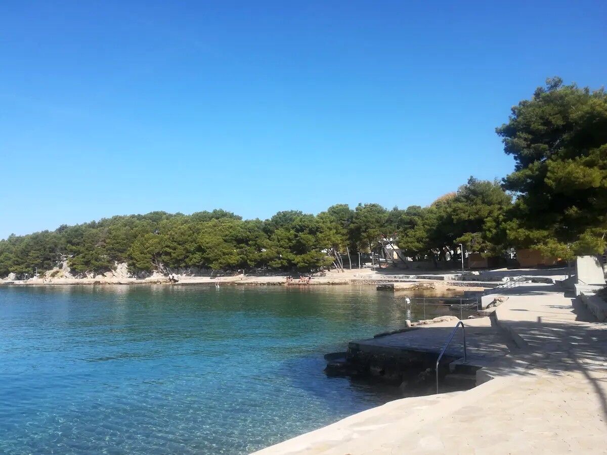 A coastal area with clear blue water, a sandy beach, and a forested hillside.