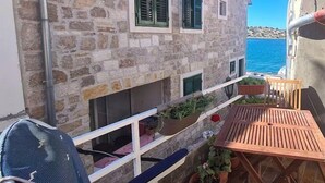 Ein Steinhaus mit einem Balkon, der auf das Meer blickt. Auf dem Balkon befinden sich ein Holztisch und Stühle.