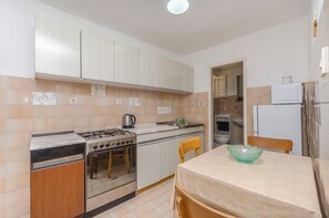 A compact kitchen with a gas stove, oven, and a microwave. There is a dining table with a bowl on it and a chair. - Apartments Nautical Nest (Tribunj)