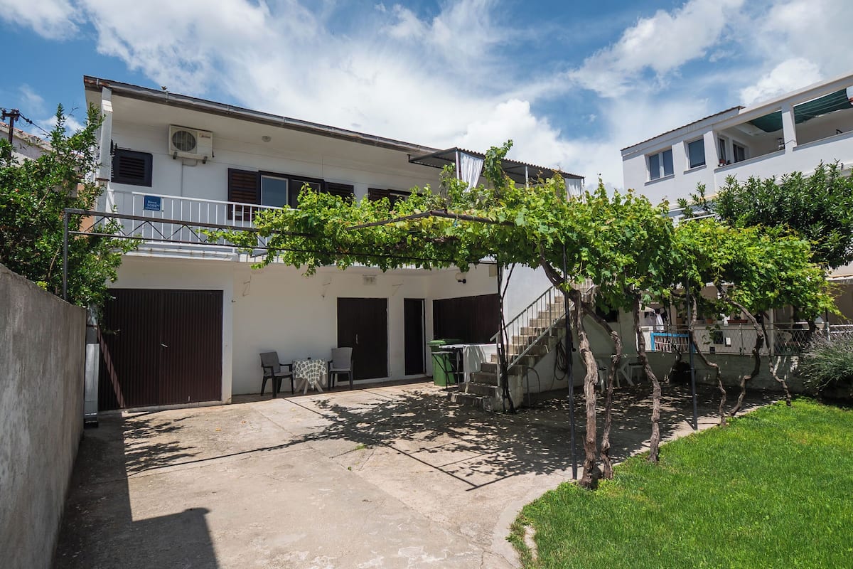 A two-story building with a covered patio area, a staircase, and a small garden with a pergola.