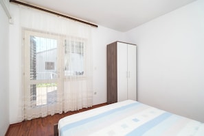 A bedroom with a bed, a wardrobe, and a window with sheer curtains. - Apartments and Room Sanja (Vodice)