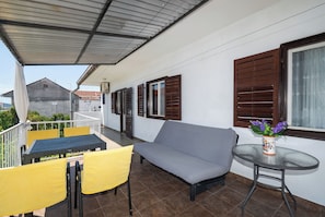 Un balcon abrité avec un canapé, des chaises jaunes, une petite table et une plante en pot.
