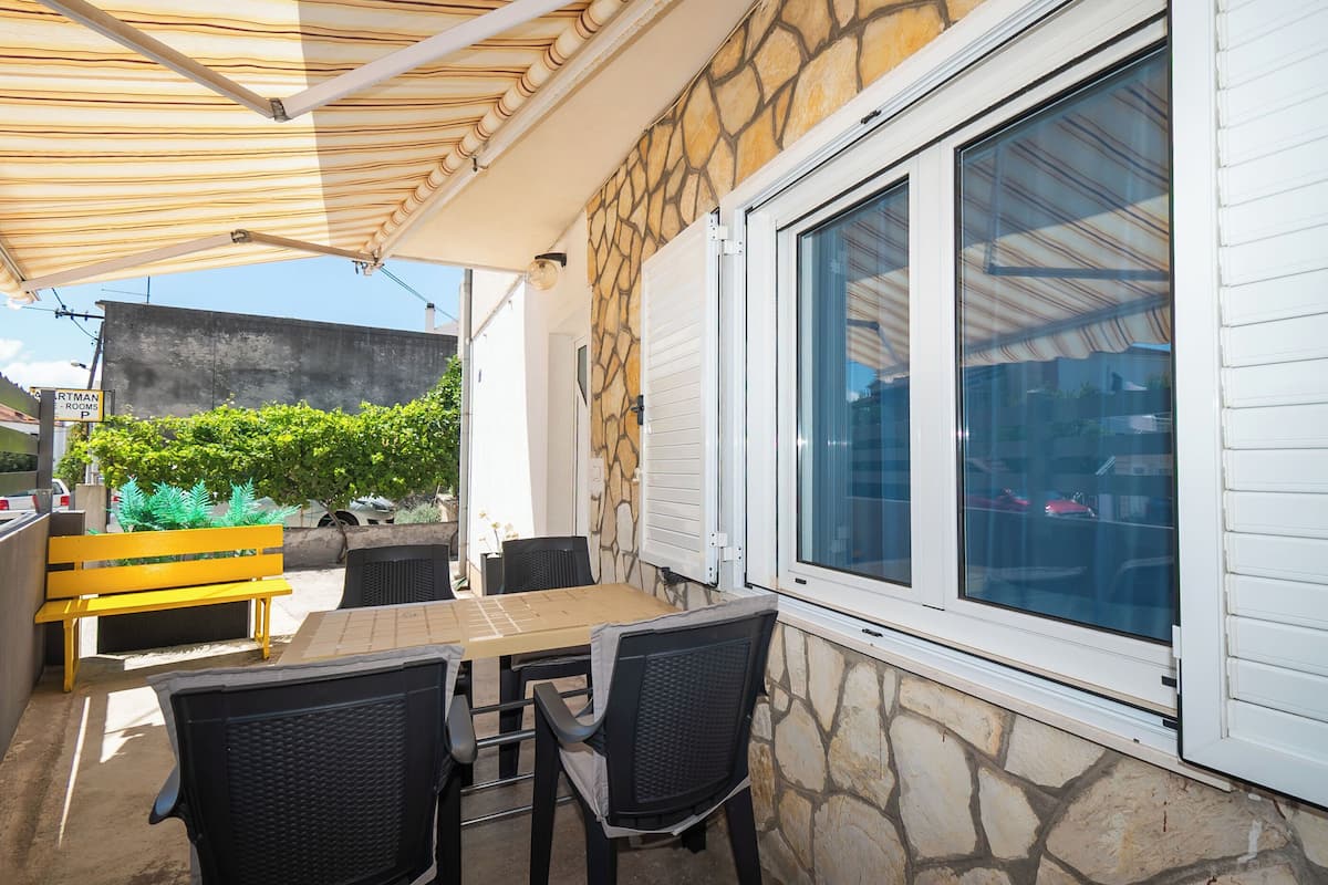 An outdoor patio with a stone wall, a wooden bench, and a table with chairs.