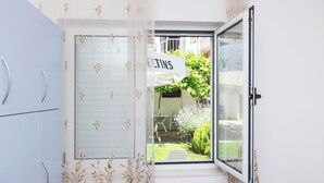 A room with a sliding glass door leading to a garden, a white cabinet, and a window with a curtain. - Apartments and Room Sanja (Vodice)