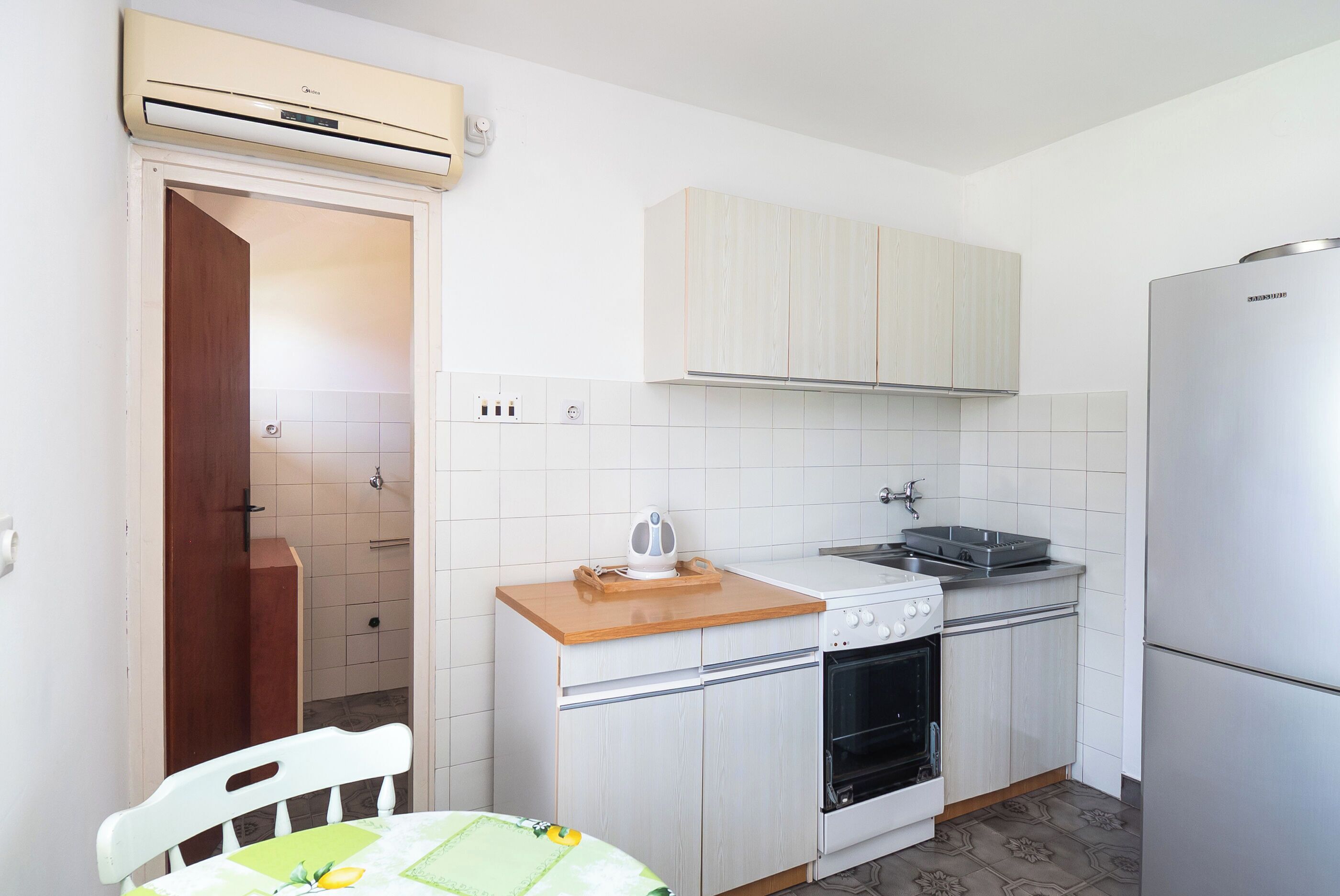 Una cocina compacta con armarios blancos, horno empotrado, lavabo y refrigerador.