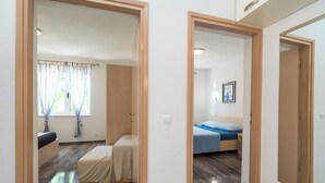 A hotel room with a bed, a small table, a chair, a window with curtains, and a wooden floor. - Apartments and Room Sanja (Vodice)