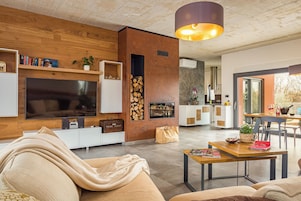 Ein modernes Wohnzimmer mit großem Flachbildfernseher, Holzpaneelen, einem Kamin und einem Essbereich mit Tisch und Stühlen.