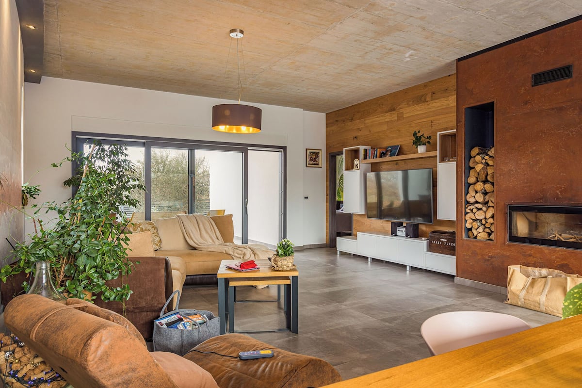 Ein modernes Wohnzimmer mit einer Couch, einem Couchtisch und einem Fernseher. Ein Kamin und ein großes Fenster sind ebenfalls vorhanden.