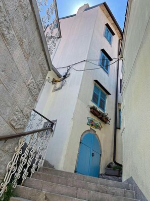 Eine enge Straße mit einer Treppe, die zu einem Gebäude mit einer blauen Tür und einem Fenster mit blauen Rollläden führt.