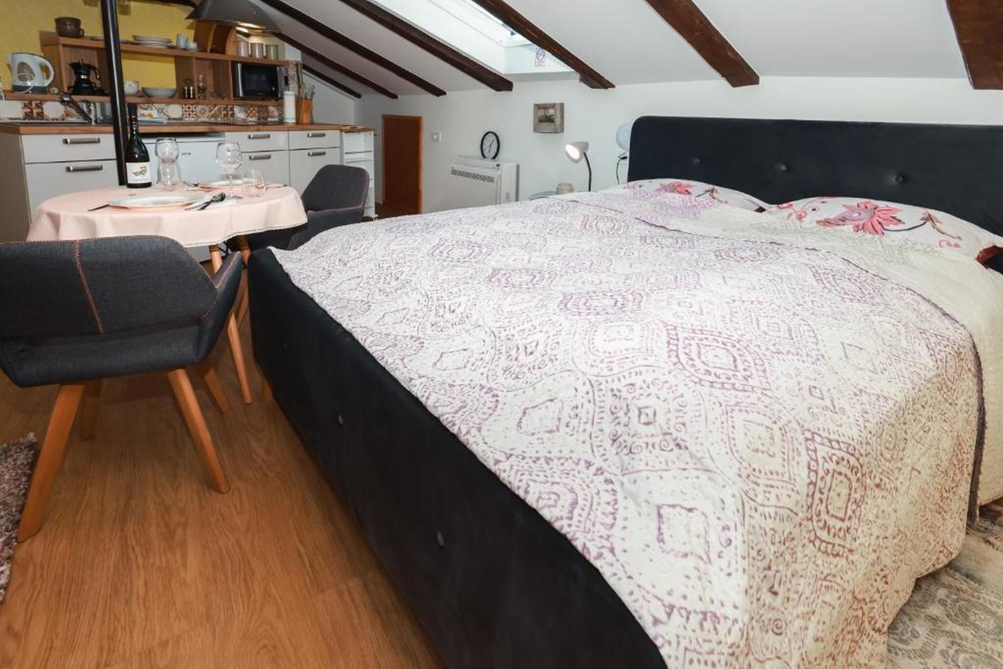 Une chambre avec un grand lit, un bureau avec une chaise, une petite table ronde et, au fond, un coin cuisine.
