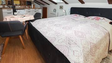 Une chambre avec un grand lit, un bureau avec une chaise, une petite table ronde et, au fond, un coin cuisine.