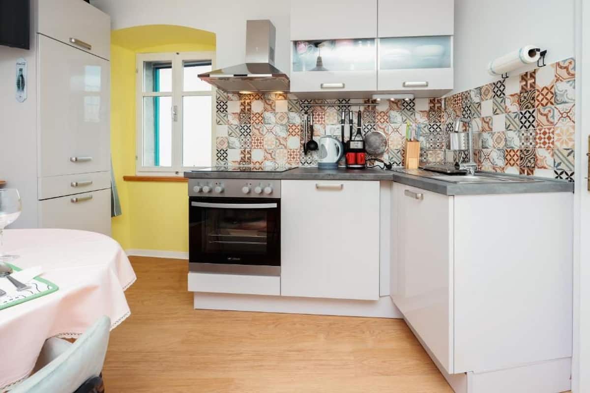 Une cuisine compacte avec des meubles blancs, un four encastré et un crédence décorée.