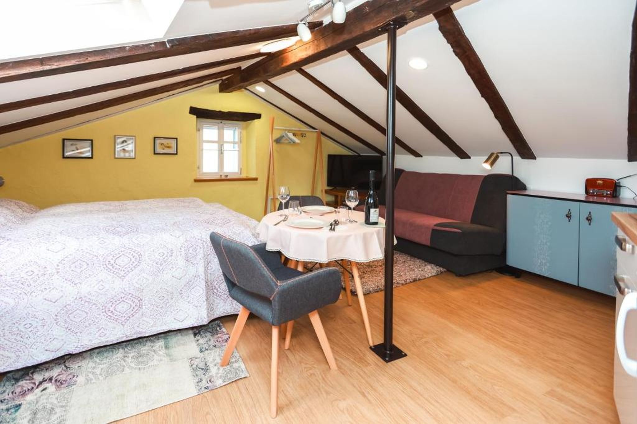 A cozy attic bedroom with a bed, a dining table, and a sofa.