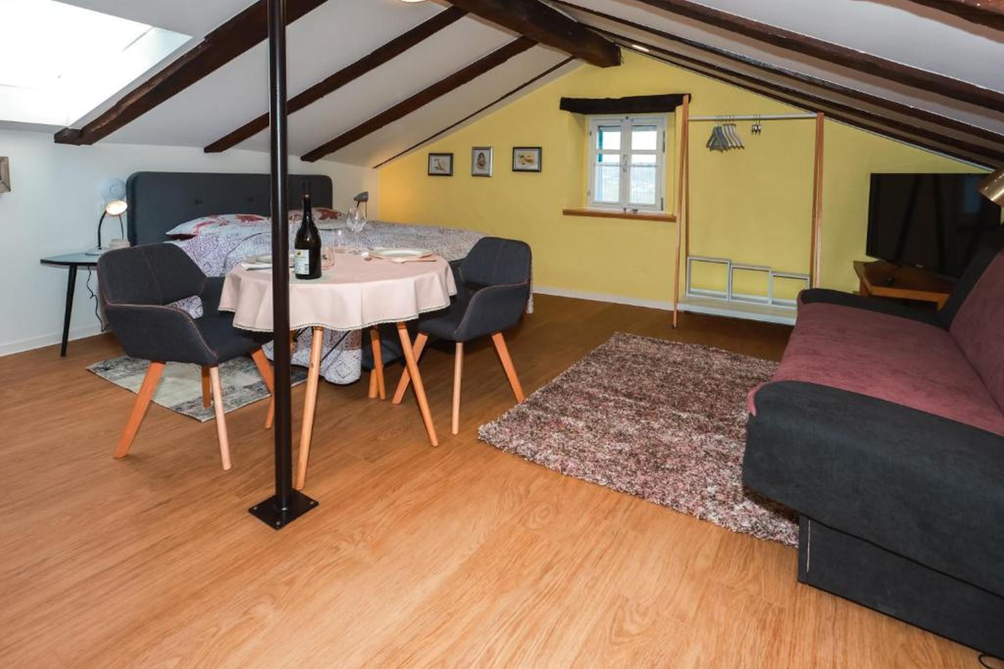 A cozy attic room with a dining table, chairs, a sofa, and a TV.