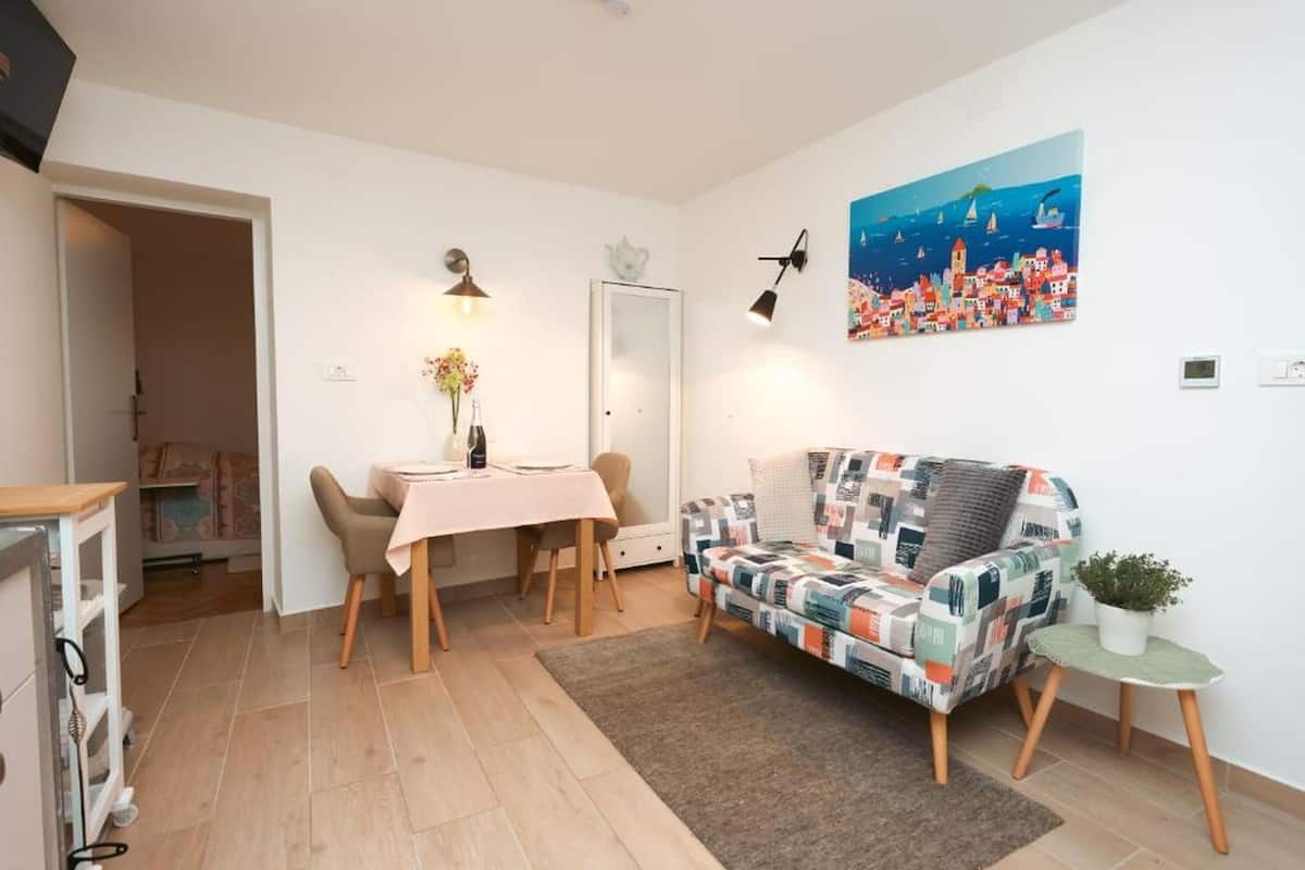 Un salon chaleureux avec un canapé à motifs, une table à manger avec des chaises, une petite table d’appoint ornée d’une plante et un tableau accroché au mur.
