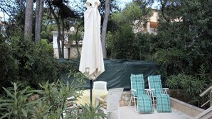 An outdoor patio with a covered seating area, surrounded by greenery and a stone wall. - Apartments Adrian (Rovinj)