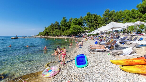 A pebbled beach with clear water, umbrellas, and beach chairs. - Apartments Adrian (Rovinj)
