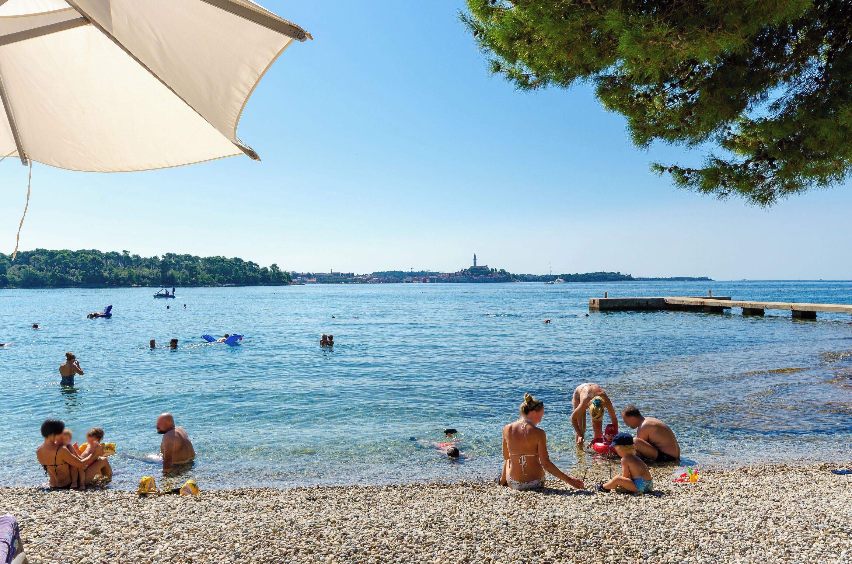 Une plage de galets où l’on peut voir des gens nager et se détendre dans l’eau.