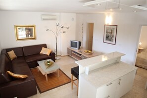 A modern living room with a brown sofa, a glass coffee table, a TV, and a kitchen area with a white countertop. - Apartments Adrian (Rovinj)