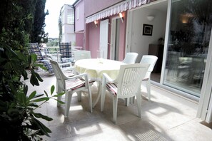 Eine Terrasse im Freien mit einem runden Tisch und weißen Stühlen, umgeben von Grünpflanzen.