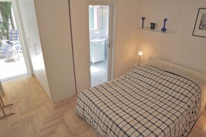 Ein Schlafzimmer mit einem Bett, einer Nachttischlampe und Blick ins Badezimmer durch eine geöffnete Tür.