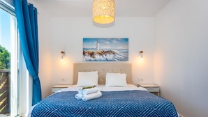 Een hotelkamer met een groot bed, een schilderij van een vuurtoren, twee nachtkastjes en een raam met gordijnen.